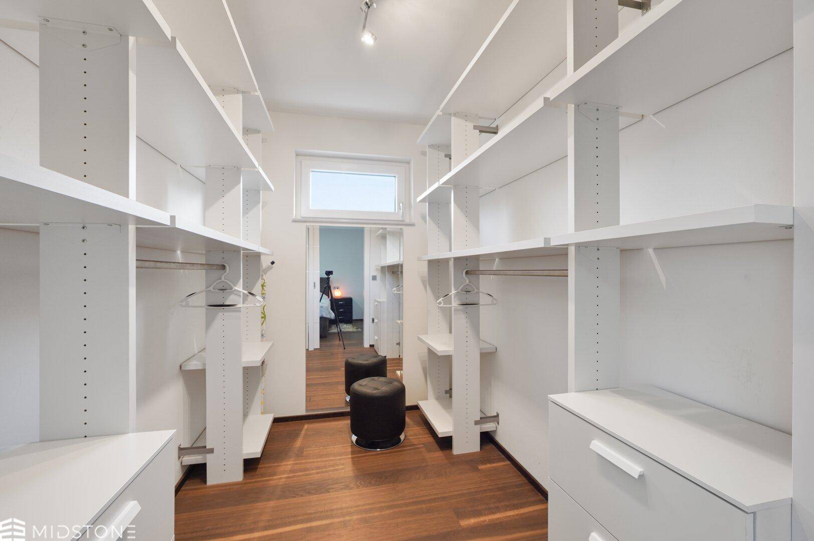 Geräumiger begehbarer Kleiderschrank mit vielen Regalen und Spiegel.