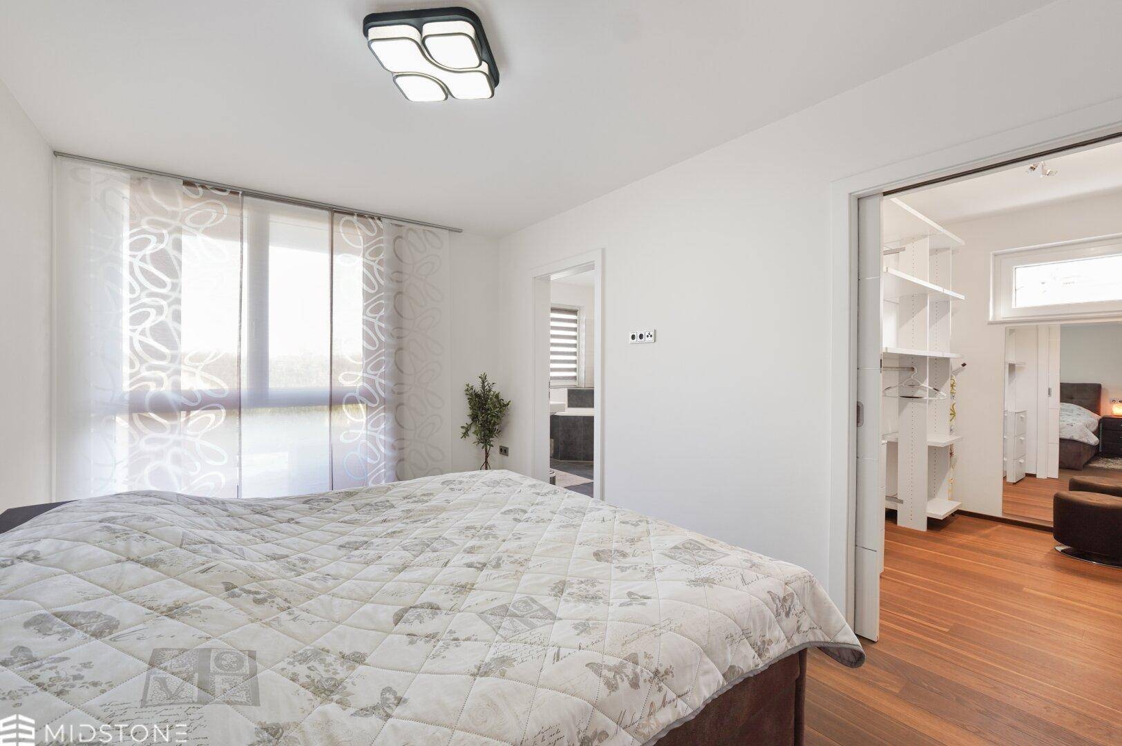 Helles Schlafzimmer mit großem Fenster und direktem Zugang zum Ankleidezimmer.