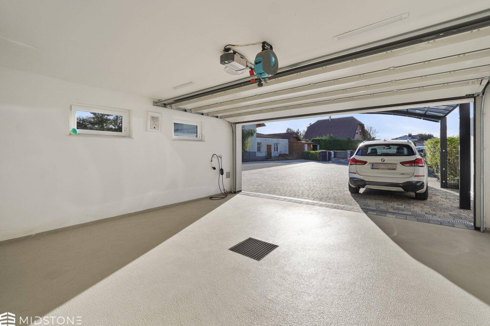 Innenansicht der Garage mit Blick auf die Auffahrt, den Carport und ein geparktes Auto.