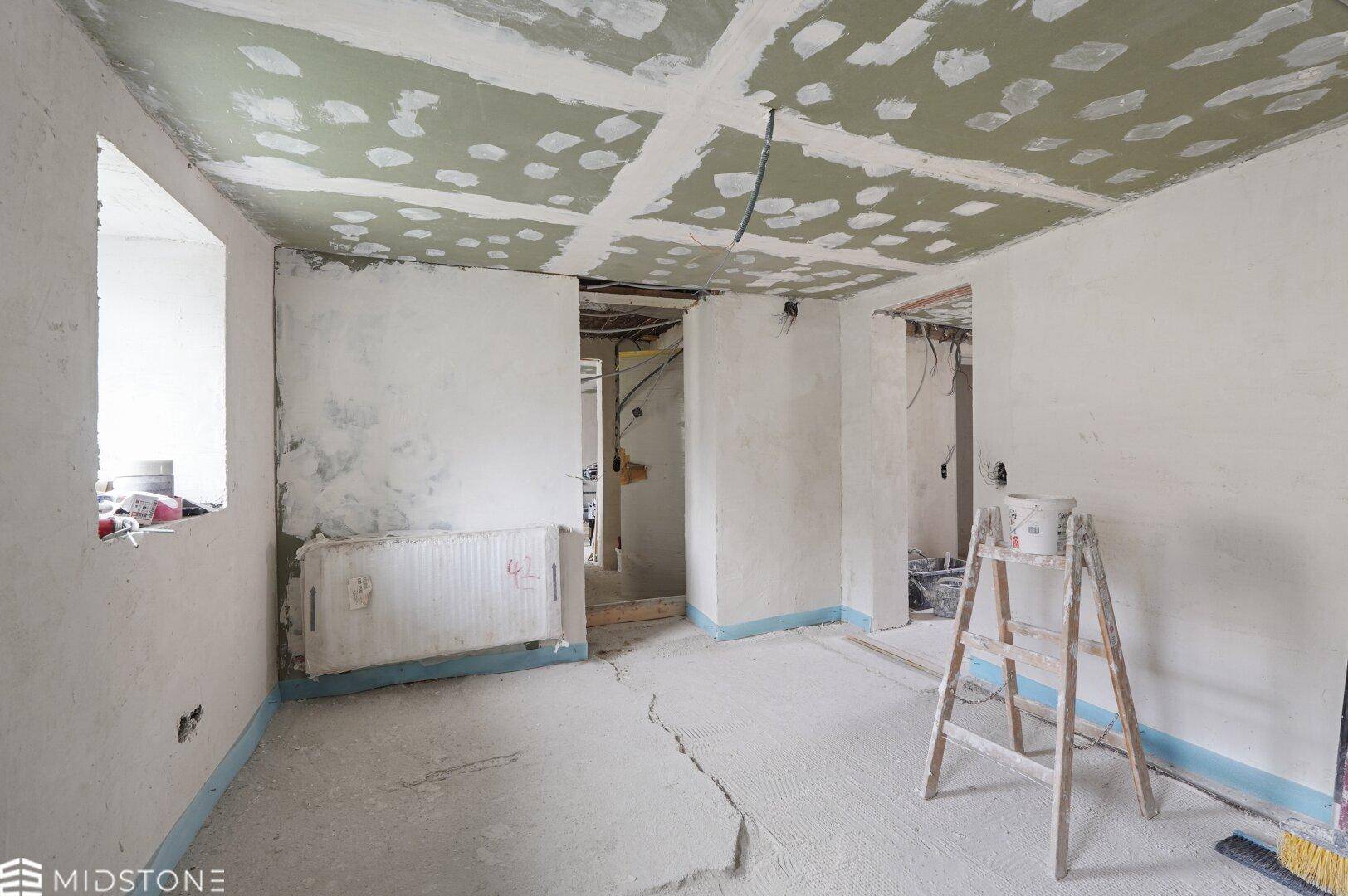 Renovierungsbedürftiger Raum mit unfertigen Wänden, Decke und Heizkörper, bereit für den Ausbau.