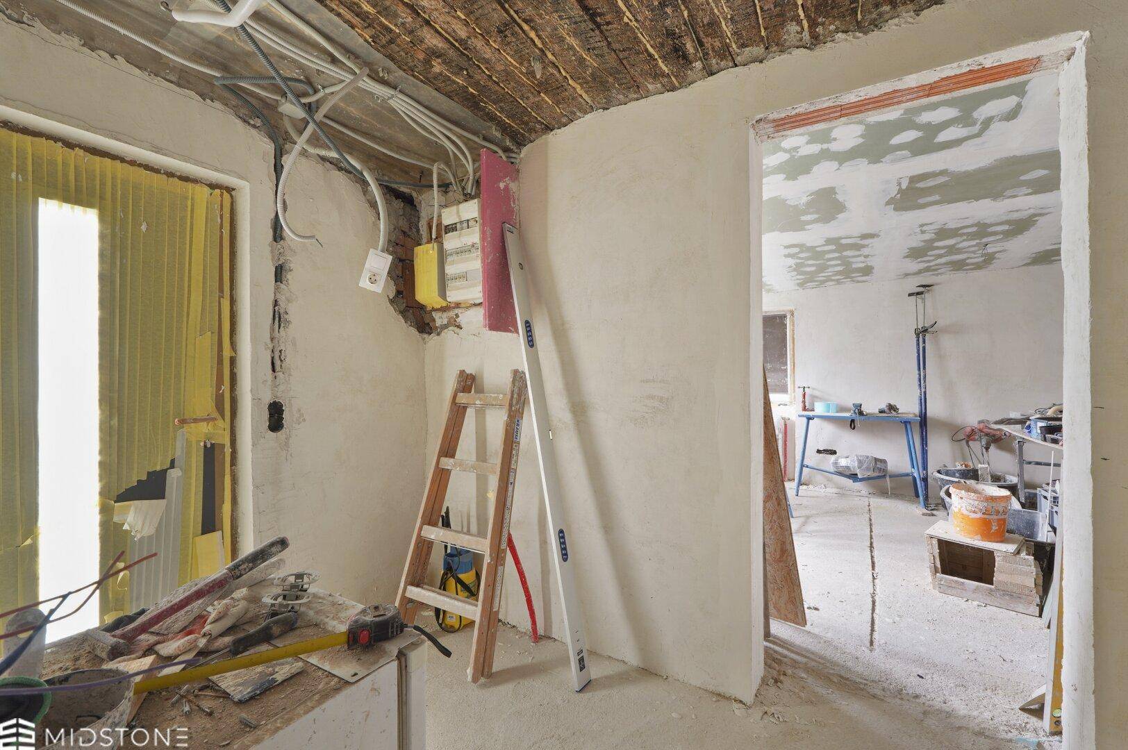 Innenbereich im Rohbau mit freiliegenden Deckenbalken, Verkabelung und Werkzeugen, bereit für den Ausbau.