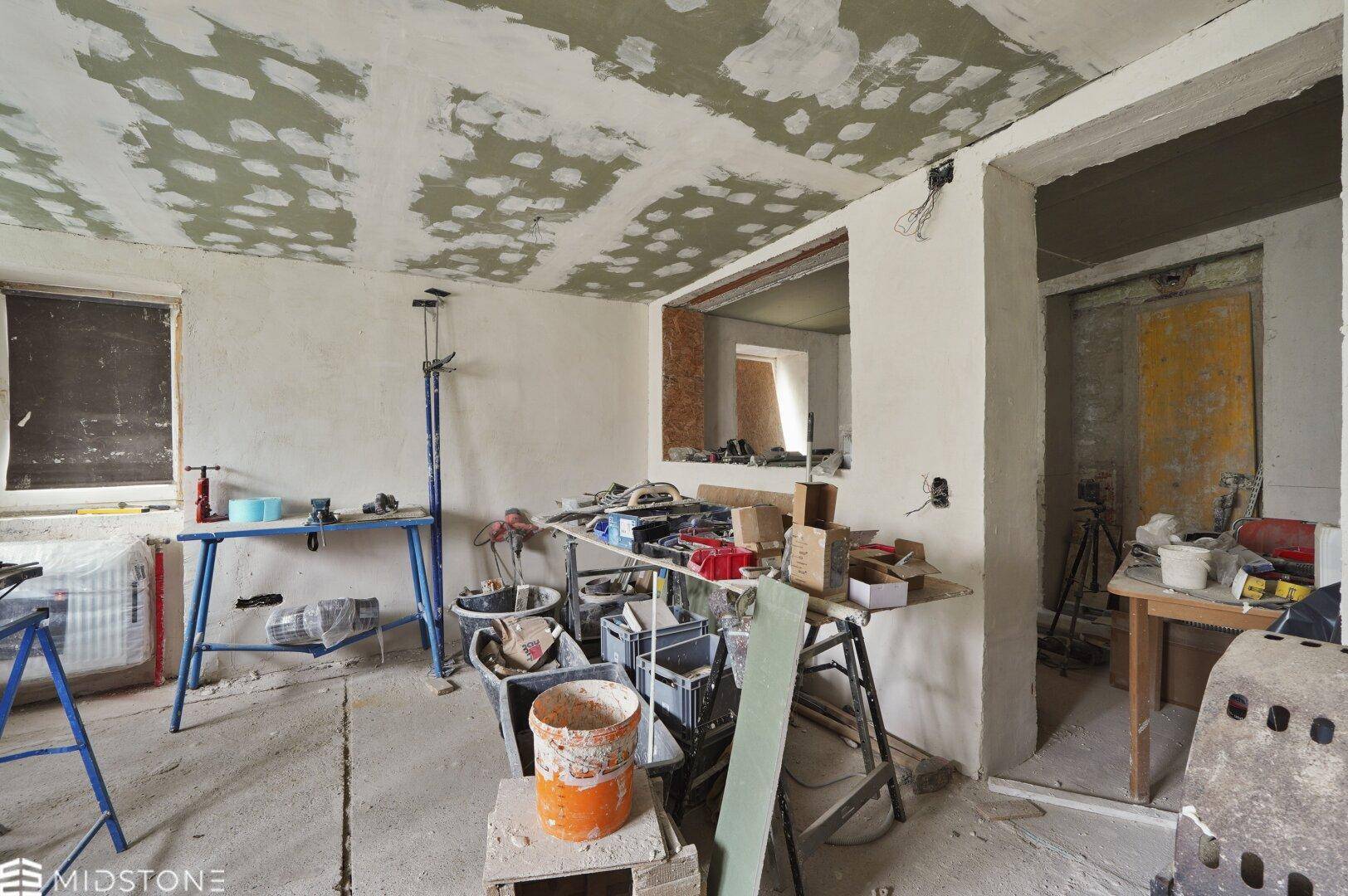 Renovierungsraum mit Werkzeugen und Baumaterialien, unfertigen Wänden und Decke, bereit für den Ausbau.