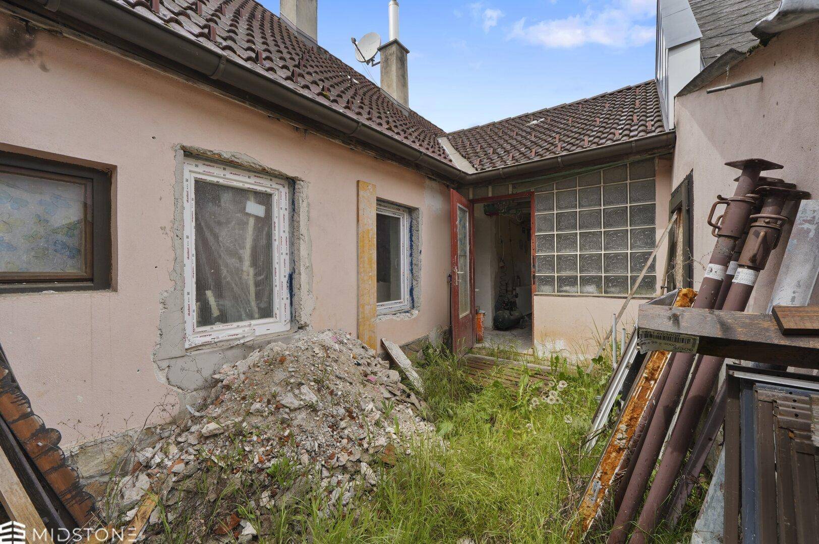 Hinterhof des Hauses mit überwuchertem Gartenbereich und Bauschutt, bereit zur Neugestaltung.