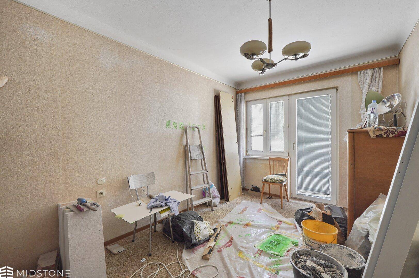 Wohnzimmer in Renovierung mit Leiter, Werkzeugen und Schutzfolie auf dem Boden.