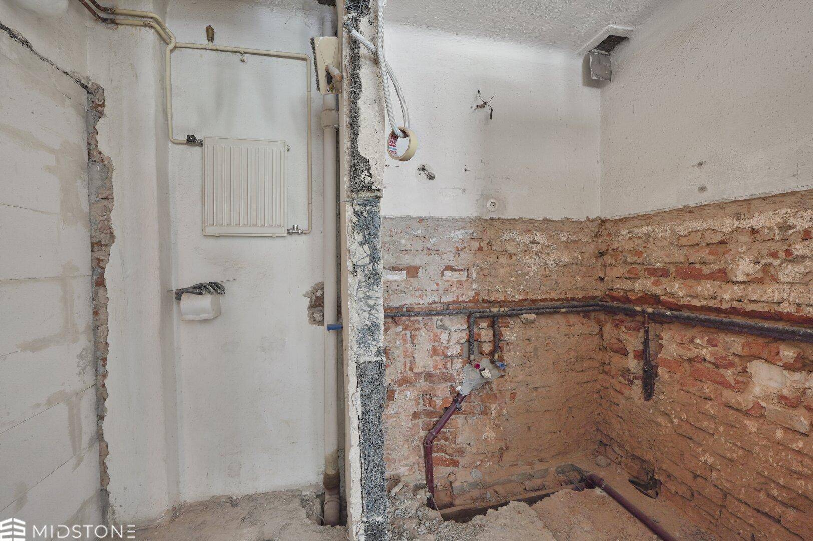 Badezimmer im Rohzustand mit freigelegten Ziegelwänden und sichtbaren Installationen, bereit zur Sanierung.