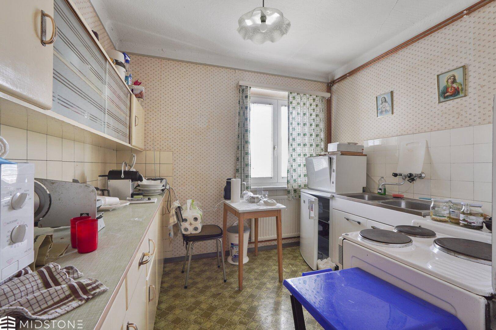 Ältere Küche mit einfachen Schränken, Spüle und Herd, bereit für eine Modernisierung.