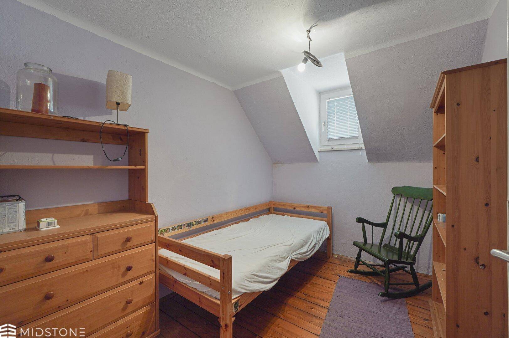 Helles Schlafzimmer im Dachgeschoss mit Holzboden, Einzelbett und Schaukelstuhl unter Dachschräge.