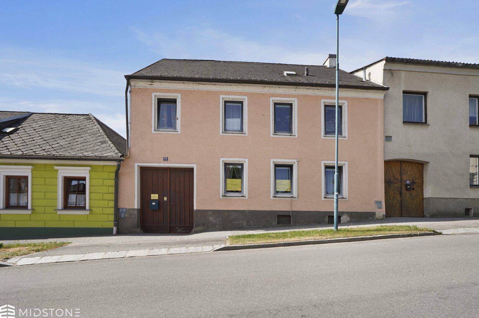 Ansicht des Wohnhauses von der Straße mit hellbrauner Fassade und angrenzenden Gebäuden.