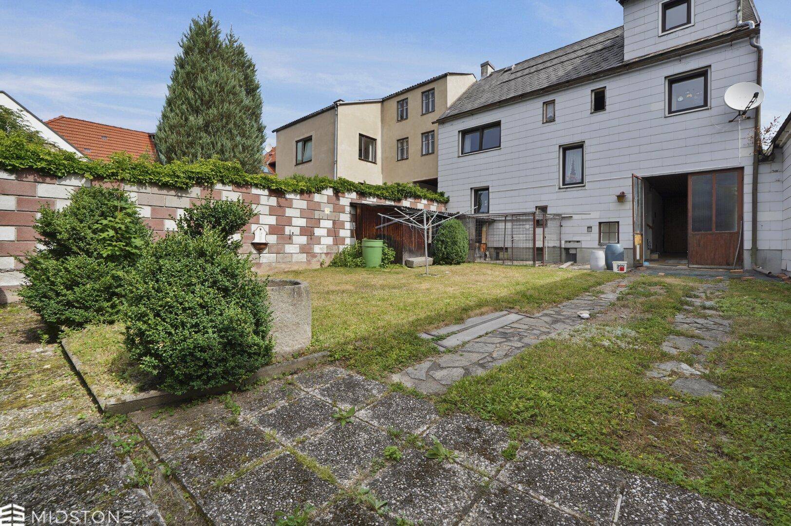 Blick auf den Garten mit Rasen, gepflastertem Weg und der Rückseite des Wohnhauses.