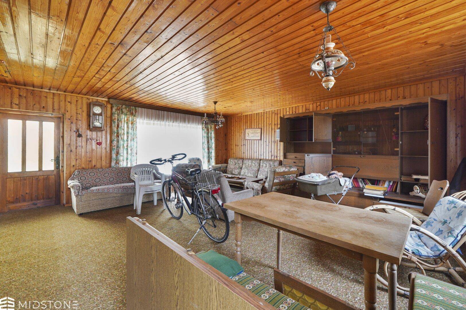 Rustikales Wohnzimmer mit Holzvertäfelung an Wänden und Decke sowie Teppichboden.