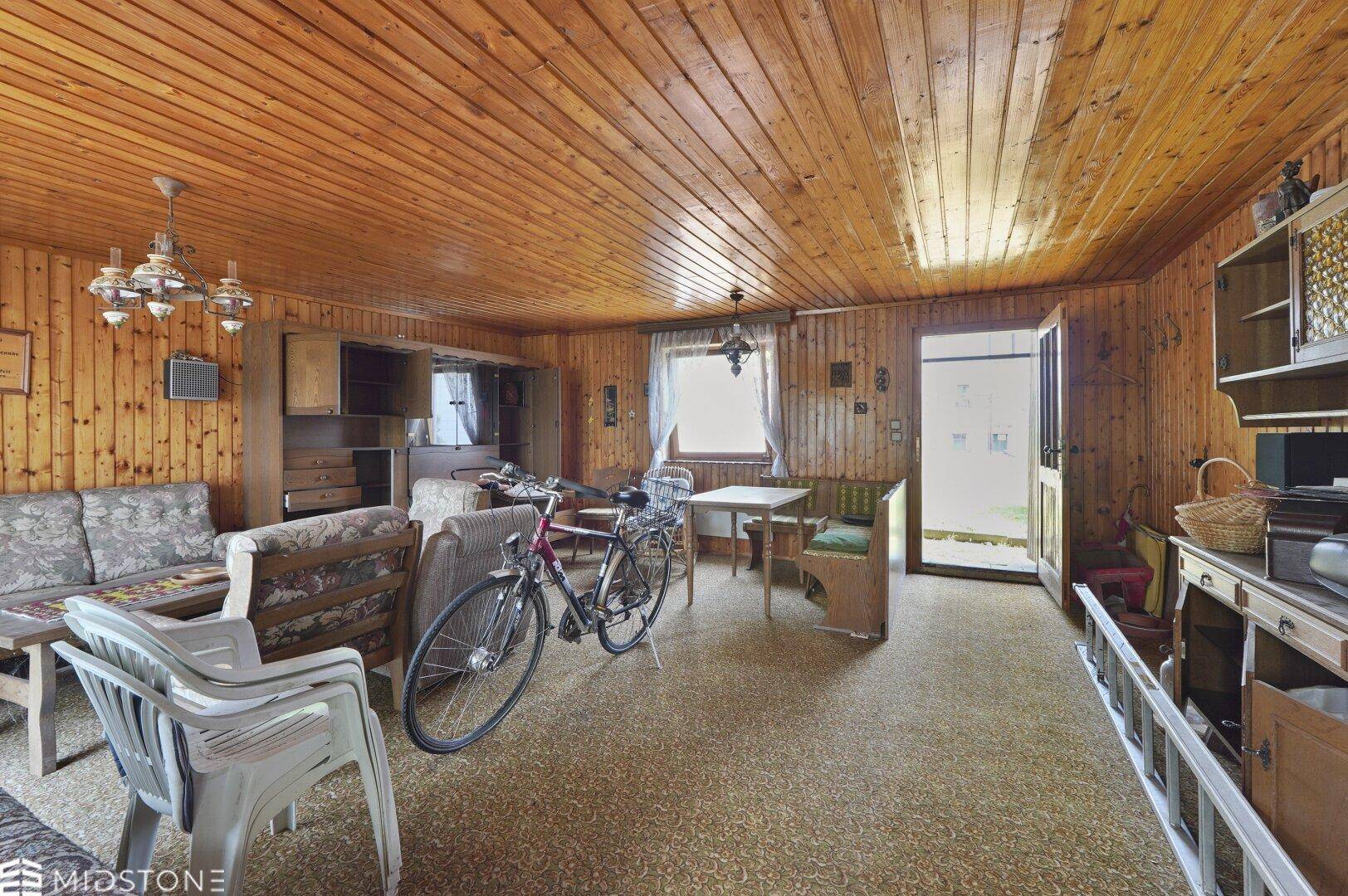 Geräumiges Wohnzimmer mit Holzvertäfelung, Teppichboden und Zugang zum Außenbereich.