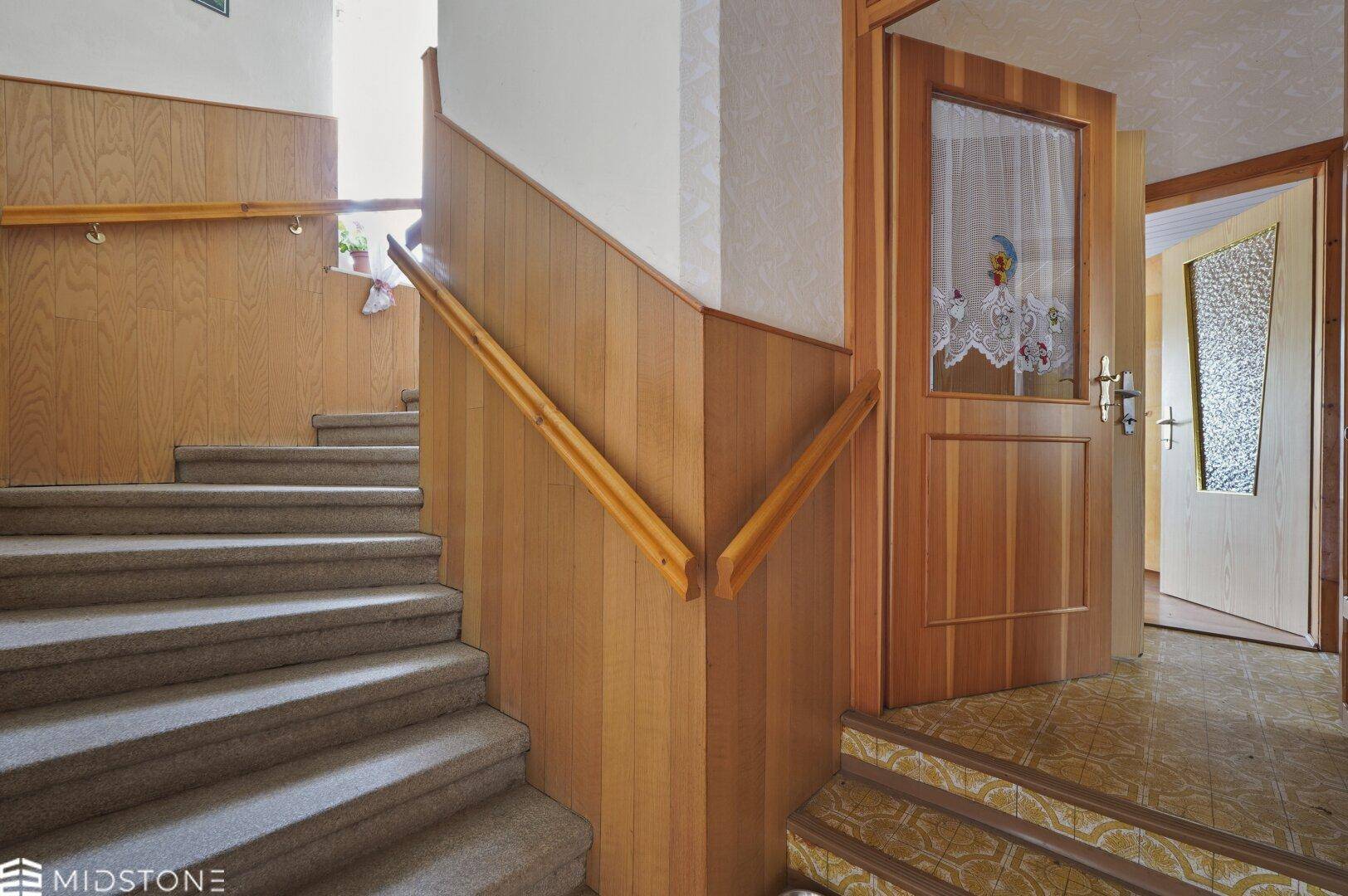 Treppenhaus mit Teppichstufen, Holzvertäfelung und Zugang zu den oberen Etagen.