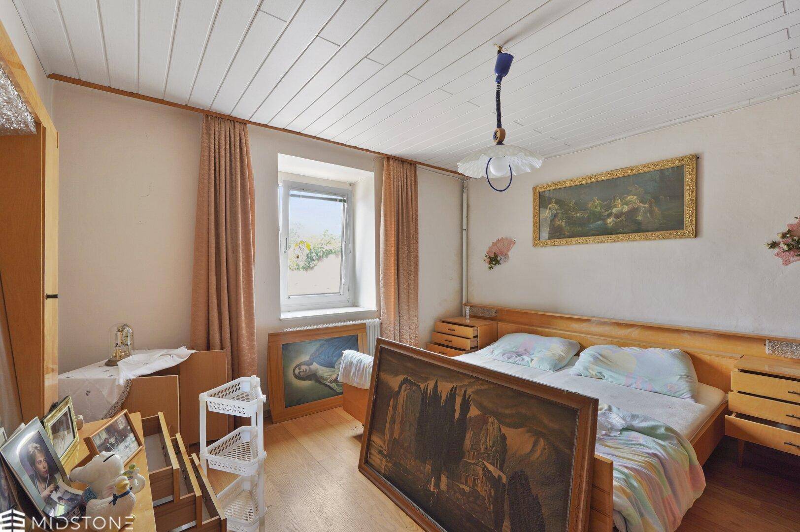 Schlafzimmer mit Holzbett, weißer Holzdecke und einem Fenster mit Blick ins Grüne.