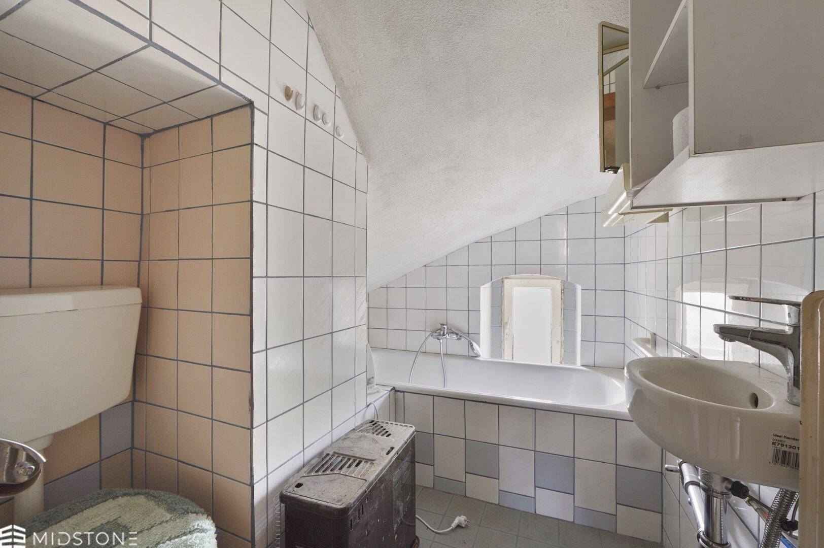 Badezimmer mit Badewanne, Waschbecken und Fliesen in Pastellfarben, unter Dachschräge.