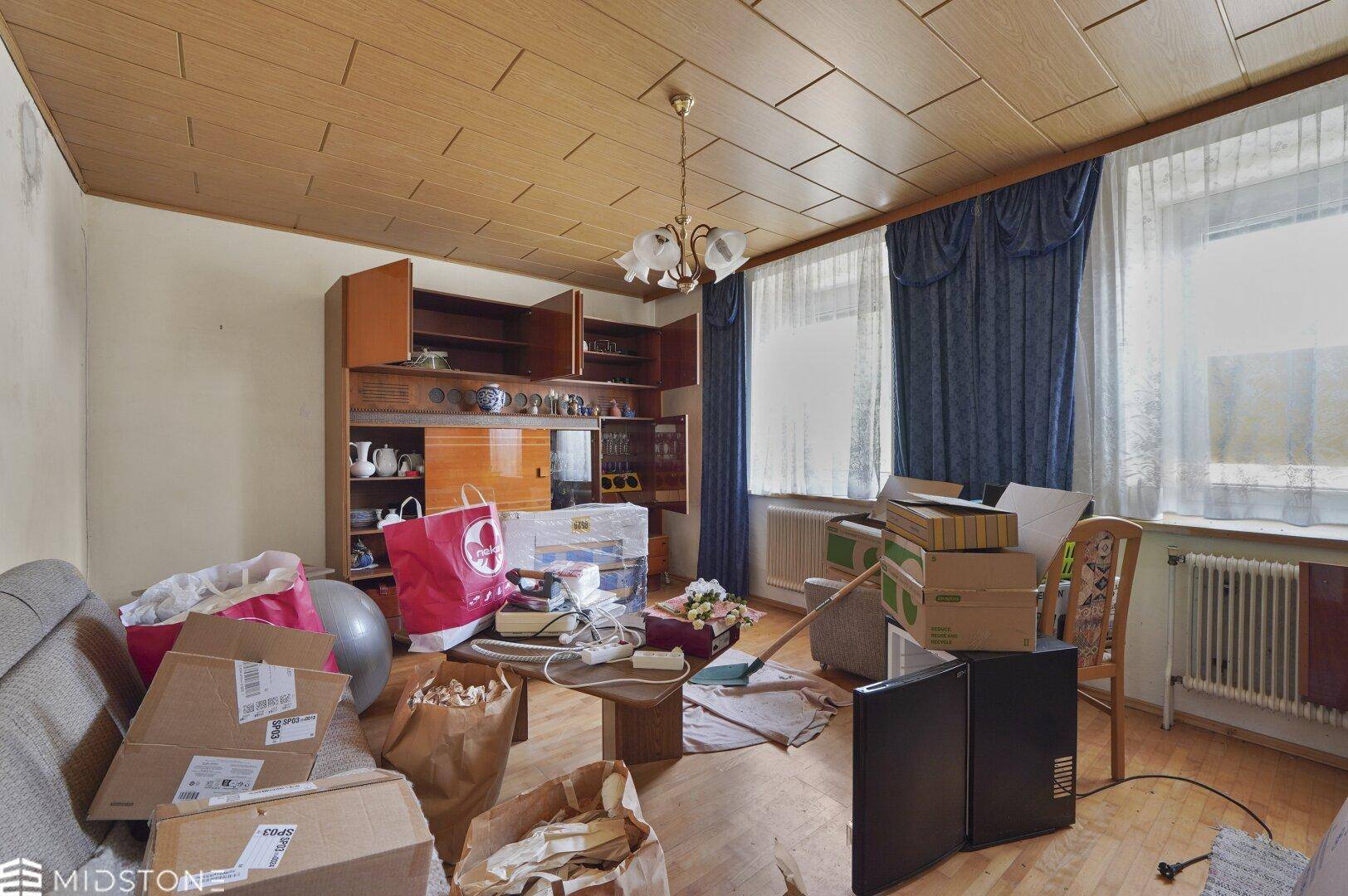 Wohnzimmer mit Holzdecke, Teppichboden und einem großen Schrank, der renovierungsbedürftig ist.