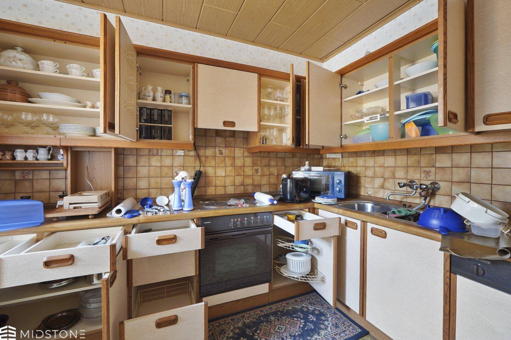 Küche mit Holzschränken, Fliesenrückwand, Spüle und integrierten Geräten.