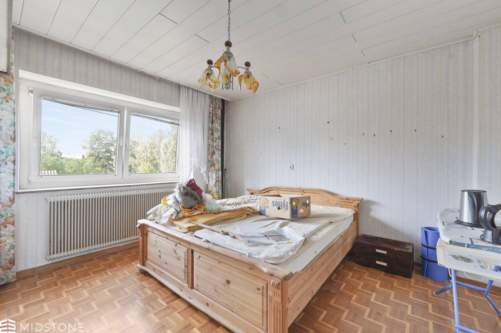 Schlafzimmer mit Holzbett, Holzdecke und einem großen Fenster mit Blick ins Grüne.