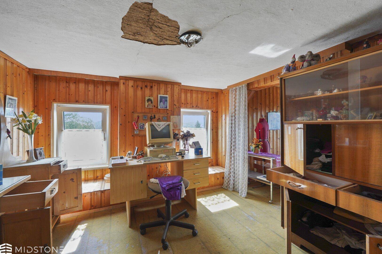 Arbeitszimmer mit Holzvertäfelung, Schreibtisch und einem beschädigten Deckenbereich.
