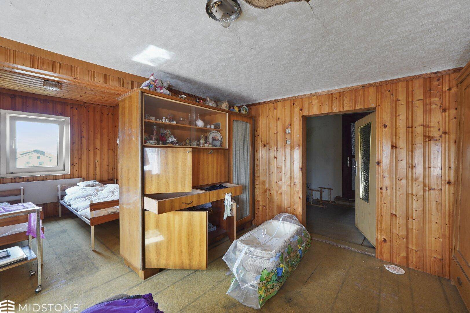 Schlafzimmer mit Holzvertäfelung, Einzelbett und einem Schrank mit Glasvitrine.