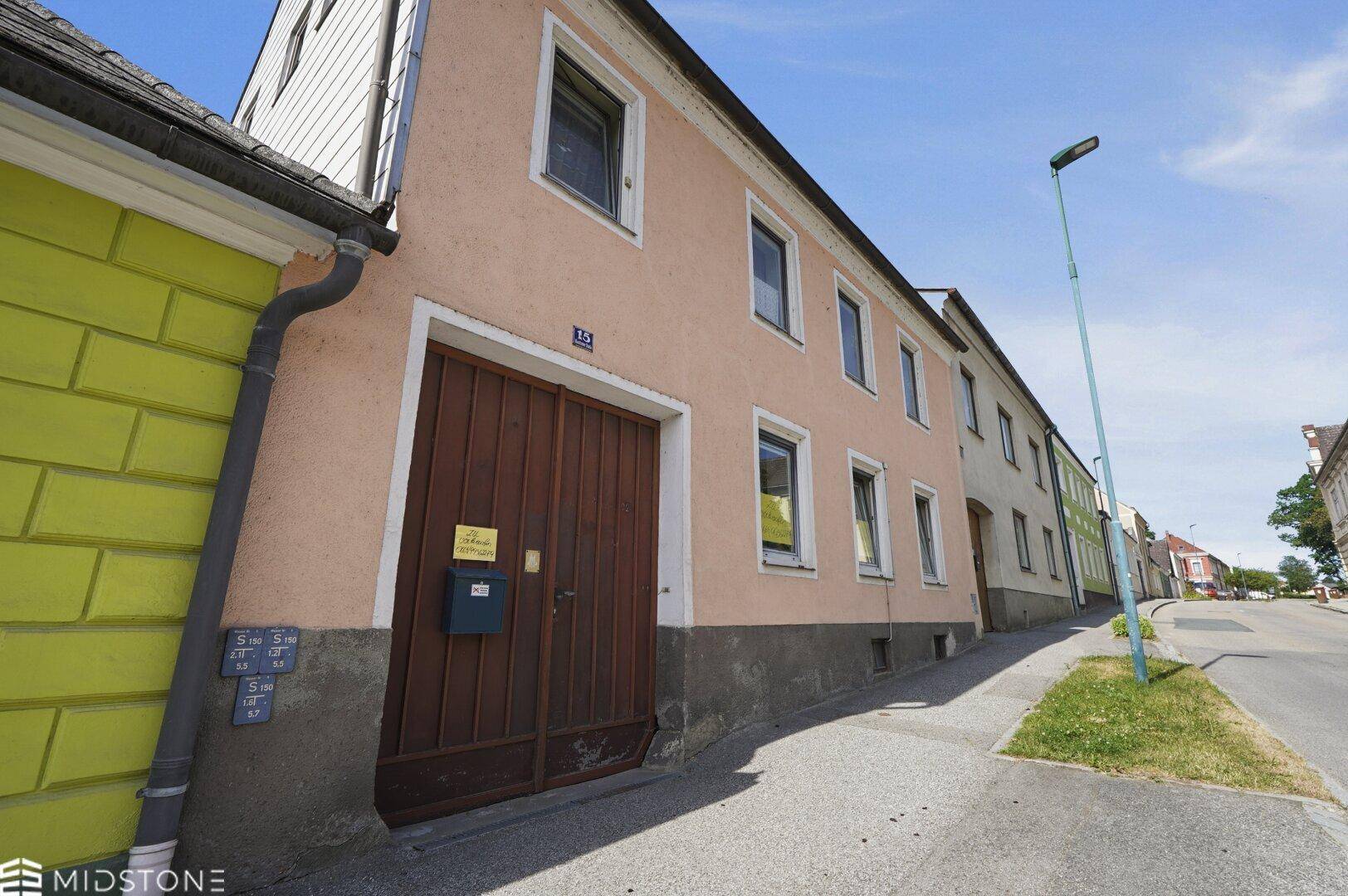 Seitenansicht des Wohnhauses mit hellbrauner Fassade und angrenzendem gelbem Gebäude.