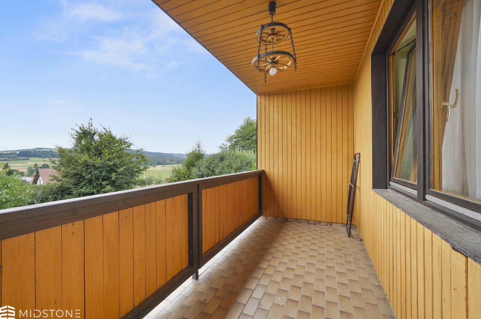 Überdachter Balkon mit Holztäfelung und weitem Blick über die Landschaft.