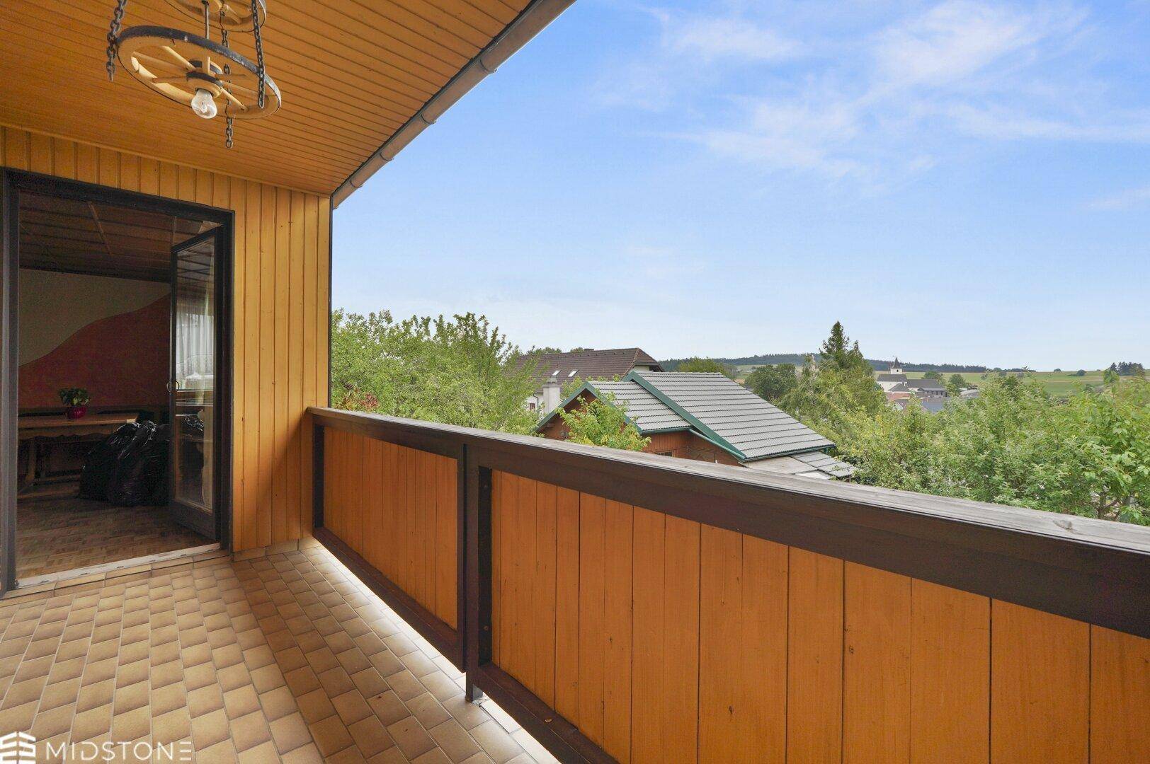 Balkon mit Fliesenboden und schöner Aussicht auf die umliegende Natur und Dächer.