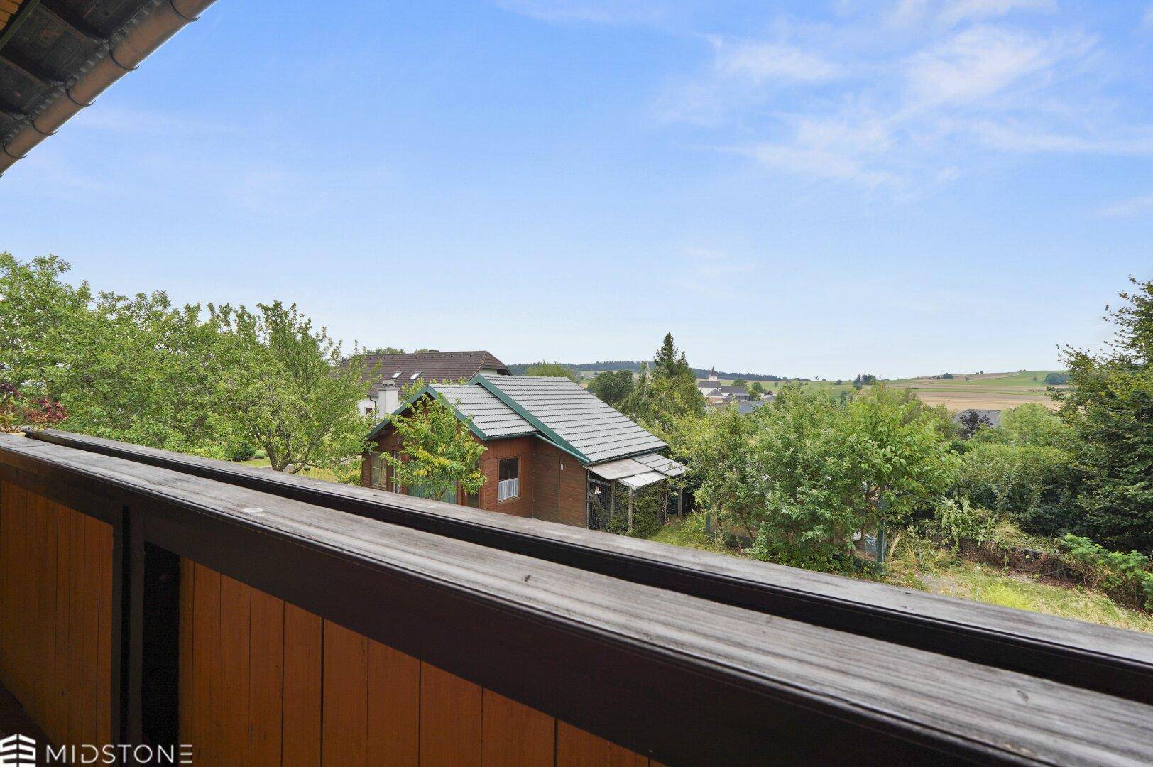 Weitläufiger Ausblick vom Balkon auf die grüne Hügellandschaft und benachbarte Häuser.