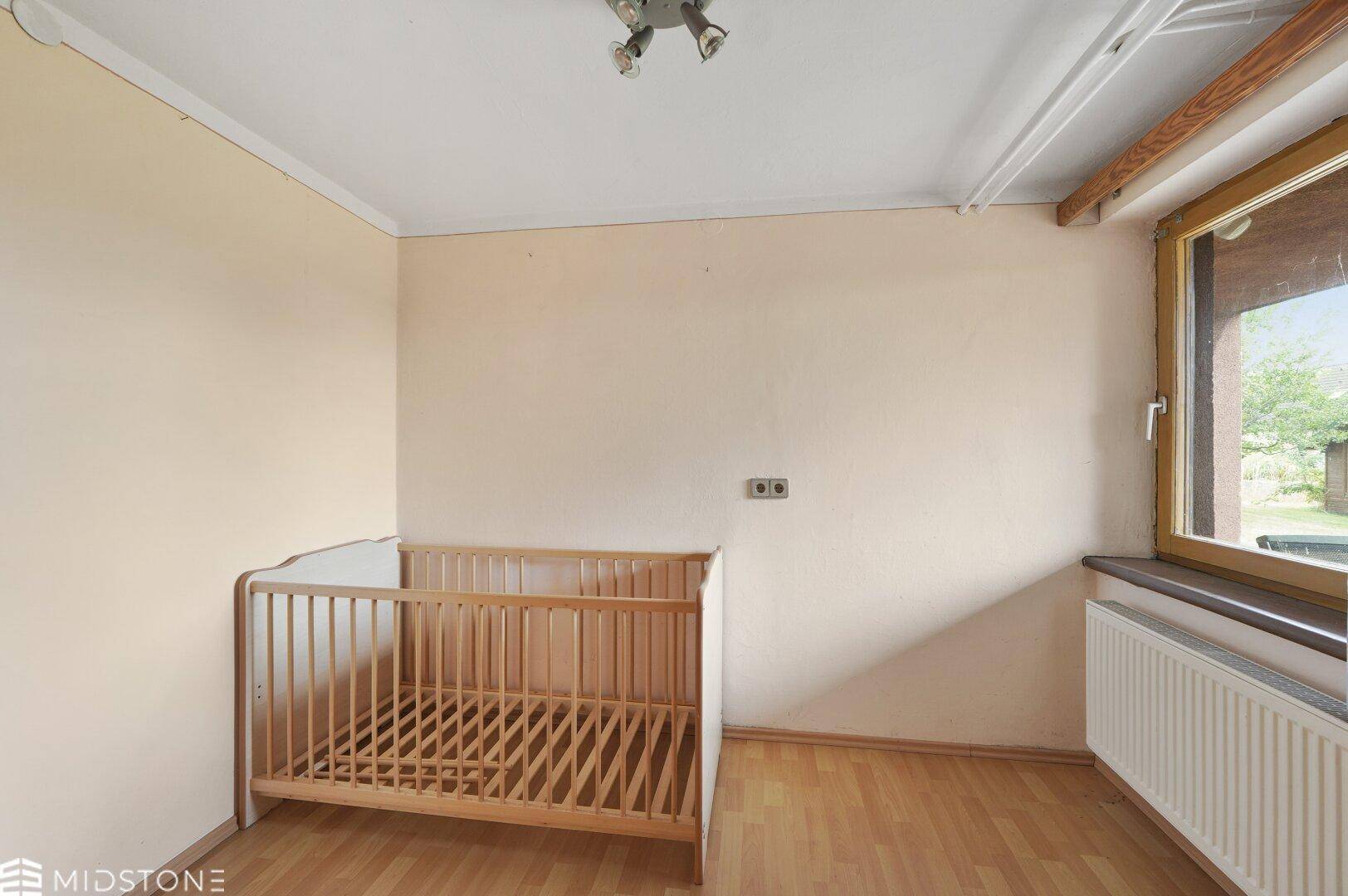 Helles Kinderzimmer mit Holzboden und Fenster, bereit zur individuellen Gestaltung.