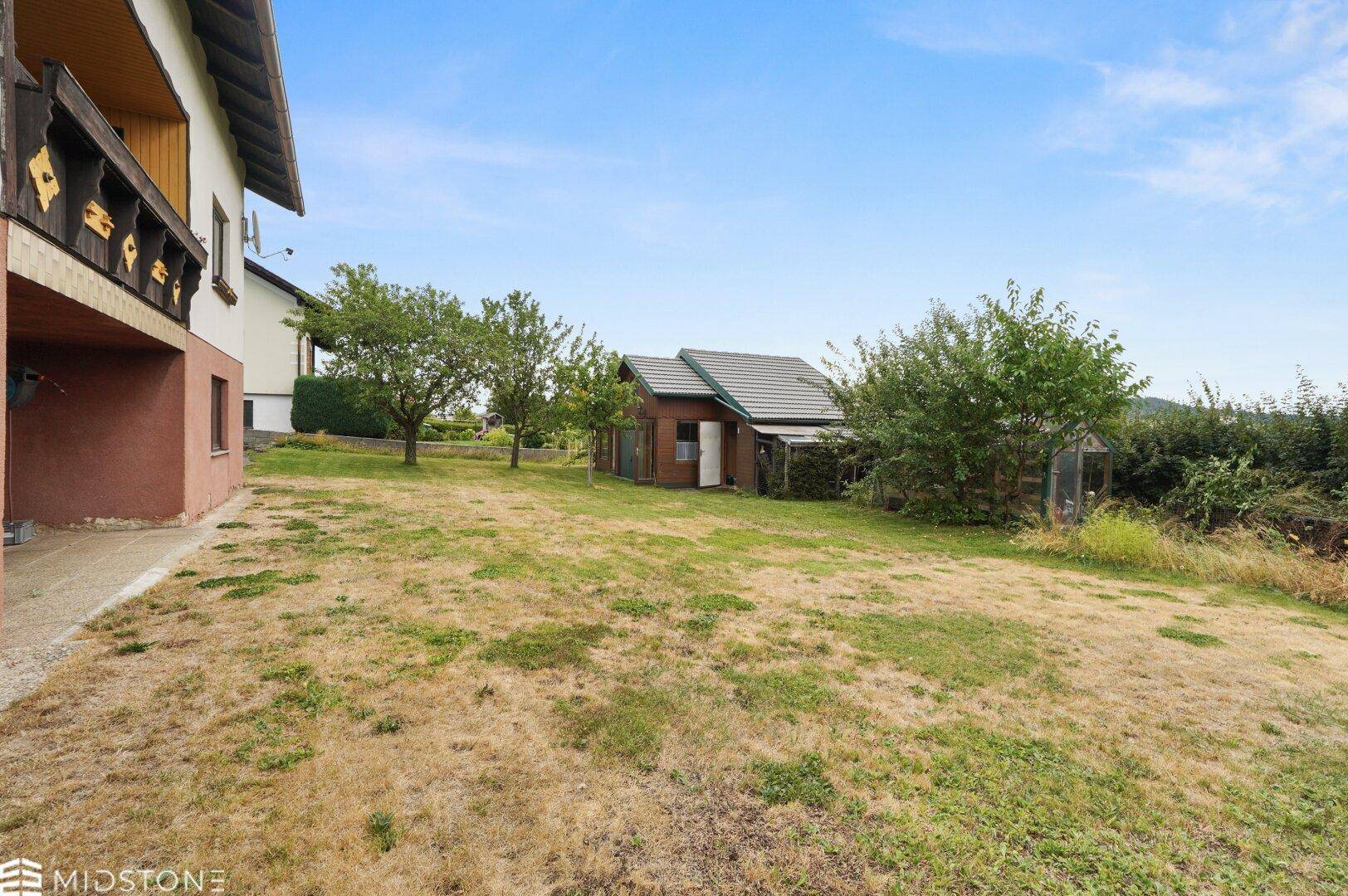 Großer Gartenbereich neben dem Haus mit Rasen und Blick auf das Gartenhaus.