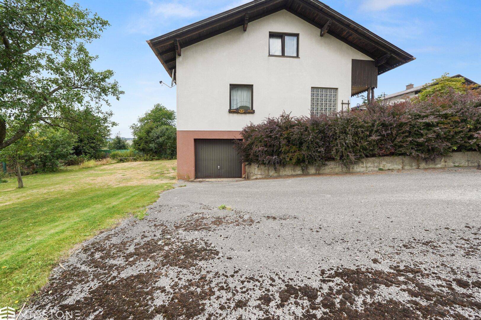 Seitenansicht des Hauses mit Garagenzufahrt und gepflegter Bepflanzung.
