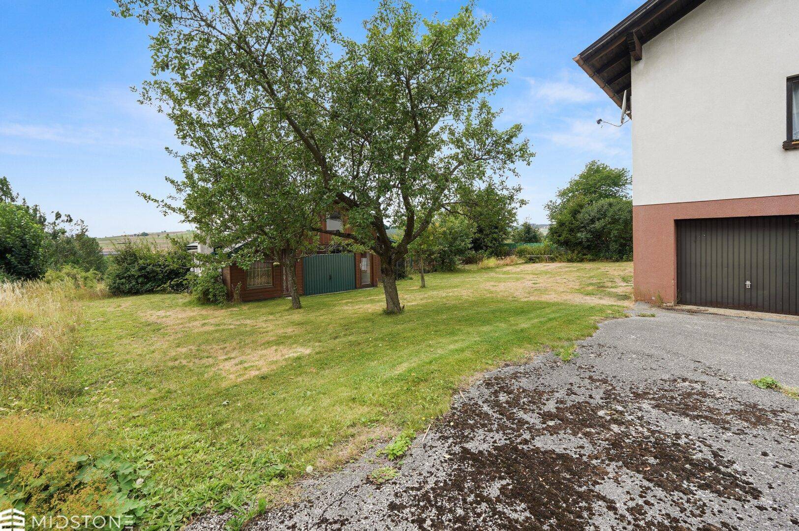 Seitenansicht des Hauses mit Garagenzufahrt und Blick auf das Gartenhaus.