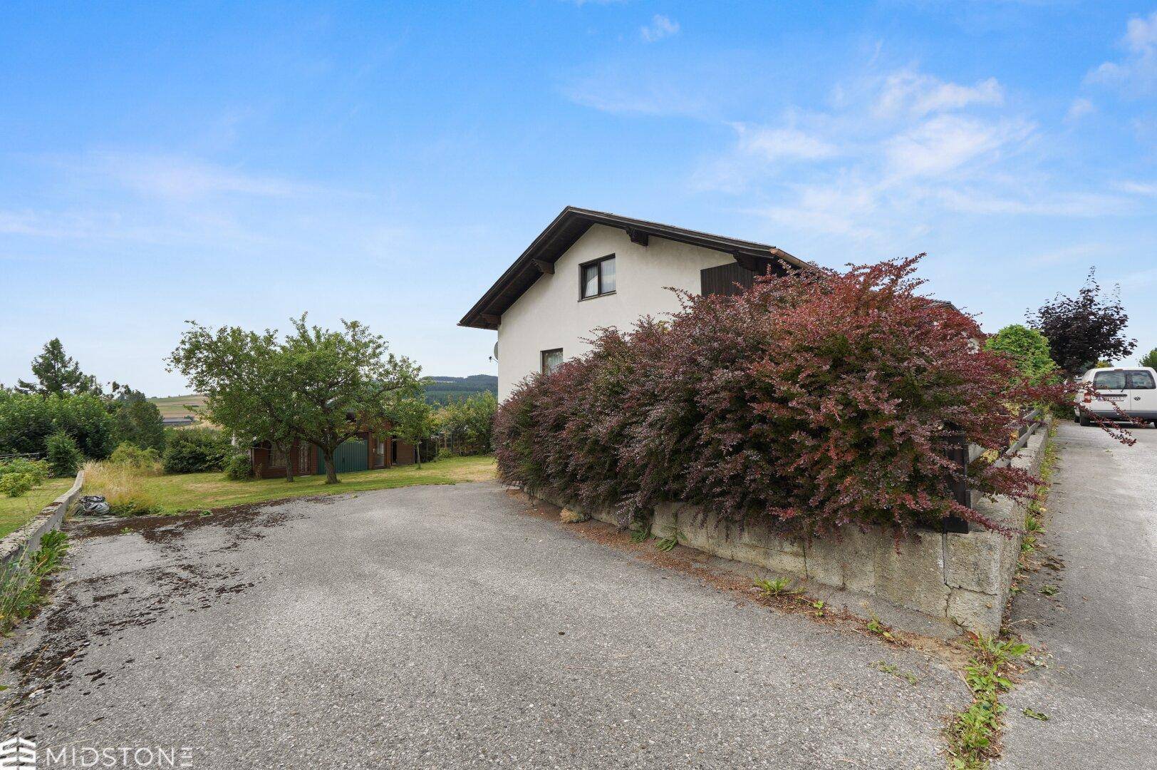 Hausansicht von der Zufahrt mit üppiger Bepflanzung und weitem Blick.