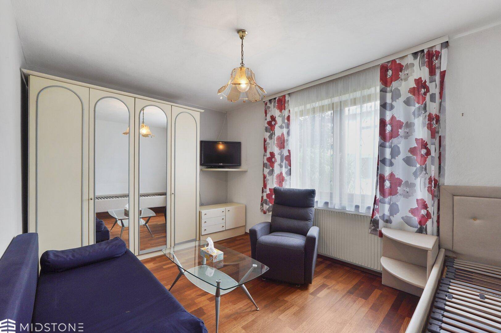 Gemütliches Schlafzimmer mit Holzfußboden, Kleiderschrank und floralen Vorhängen.