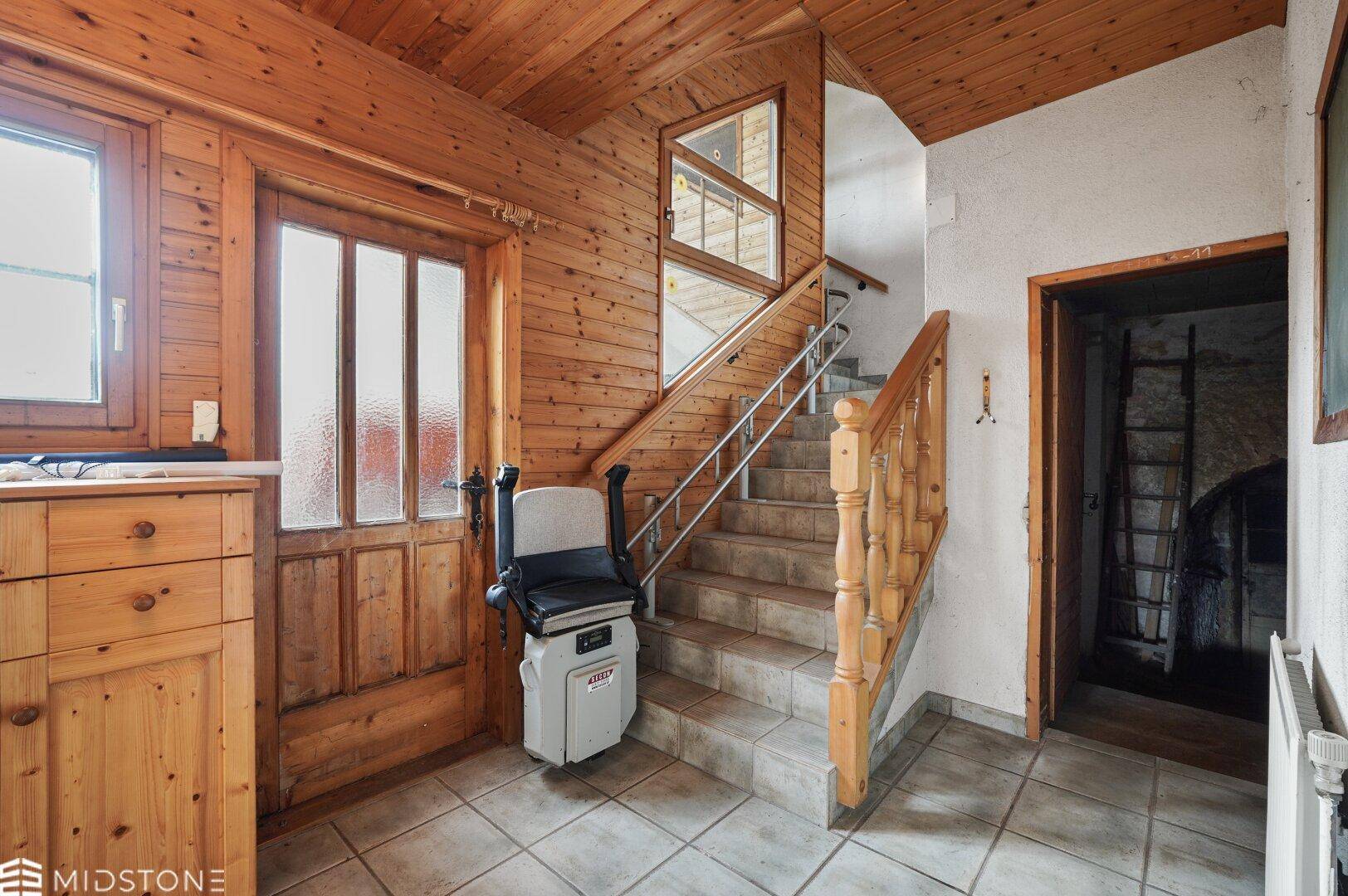 Rustikaler Eingangsbereich mit Holzvertäfelung, gefliestem Boden und Treppenlift zur oberen Etage.