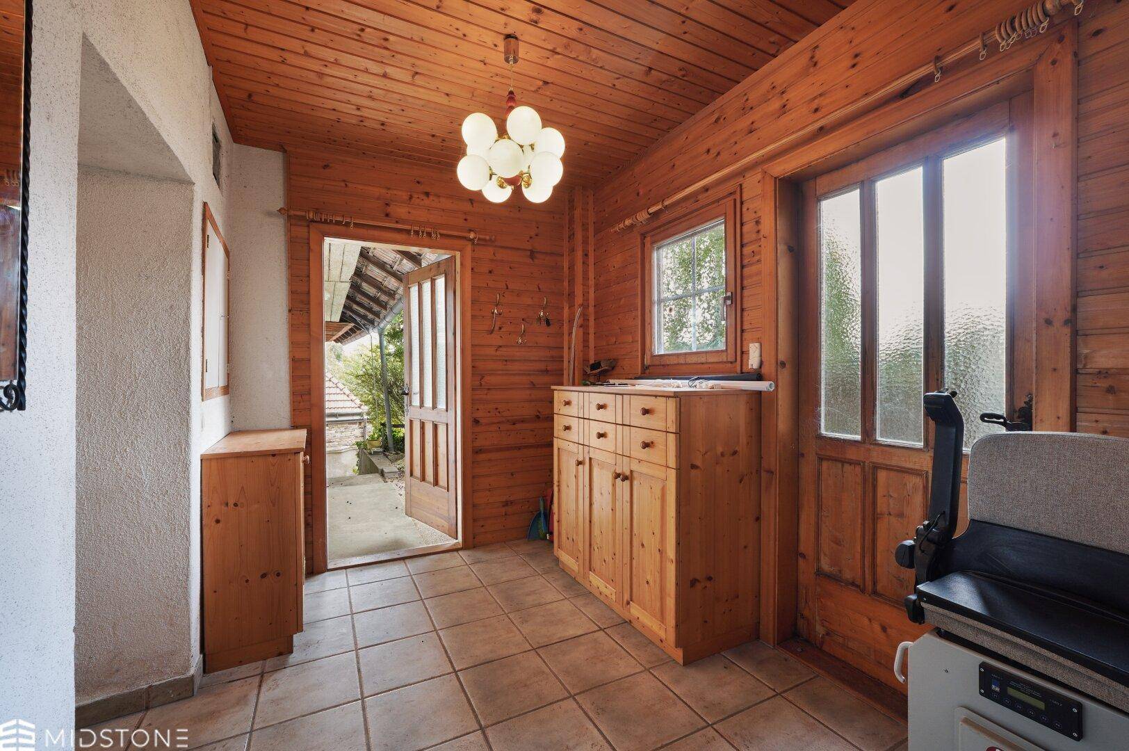 Gemütlicher Flur mit Holzverkleidung, Fliesenboden und Zugang zu einem überdachten Außenbereich.