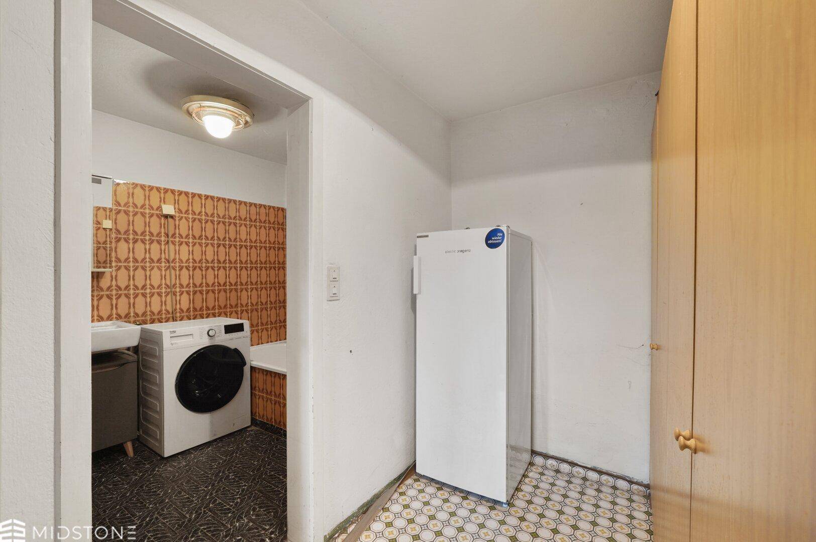Hauswirtschaftsraum mit Waschmaschine, Kühlschrank und Zugang zu einem gefliesten Badezimmer.