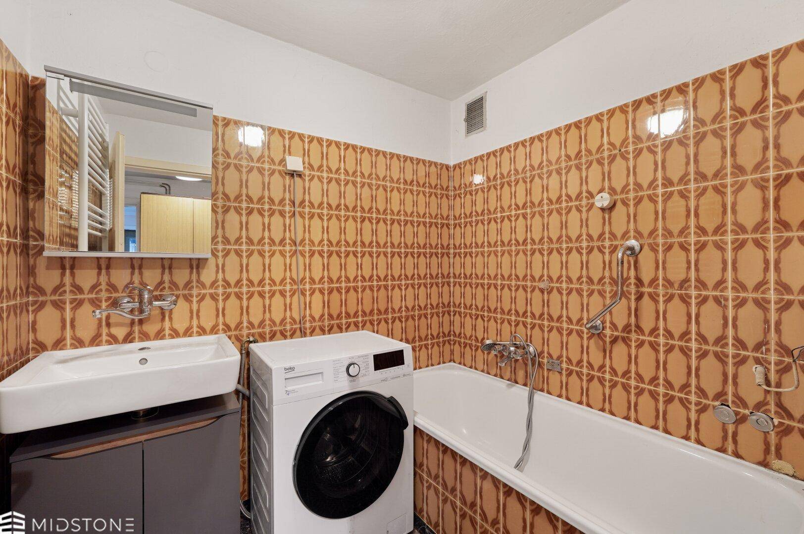 Badezimmer mit Badewanne, Waschbecken und Waschmaschine, ausgestattet mit braunen Retro-Fliesen.