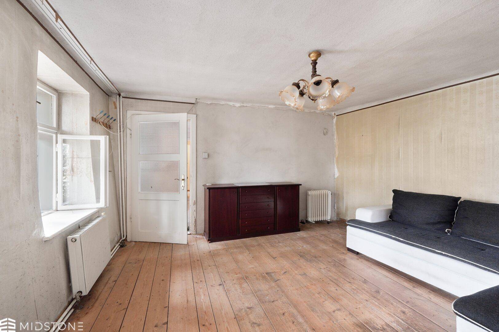 Geräumiges Wohnzimmer mit Dielenboden, Fenster und einem dunklen Holzschrank.