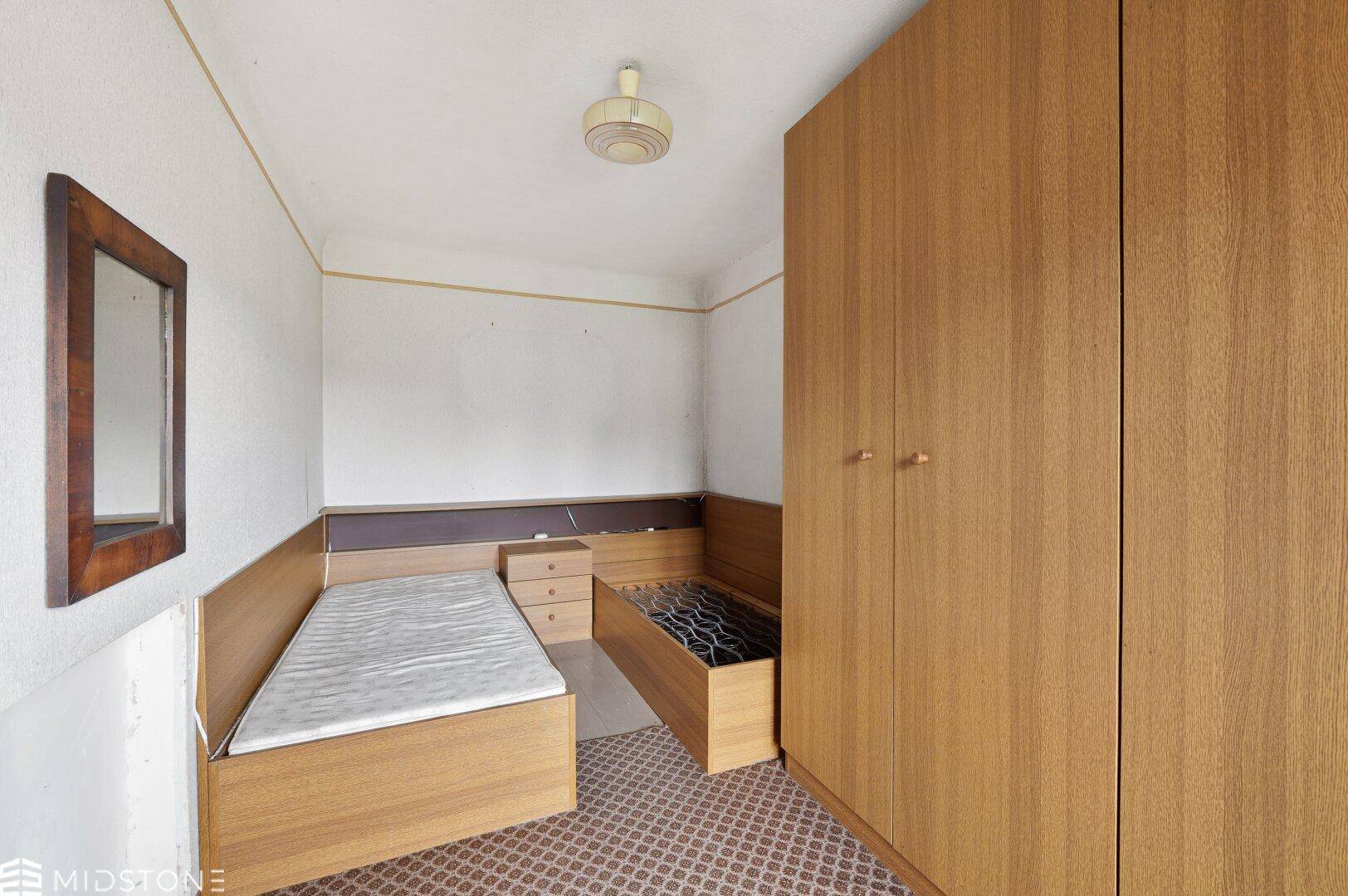 Schlafzimmer mit zwei Einzelbetten und einem großen Holzschrank, ausgestattet mit Teppichboden.