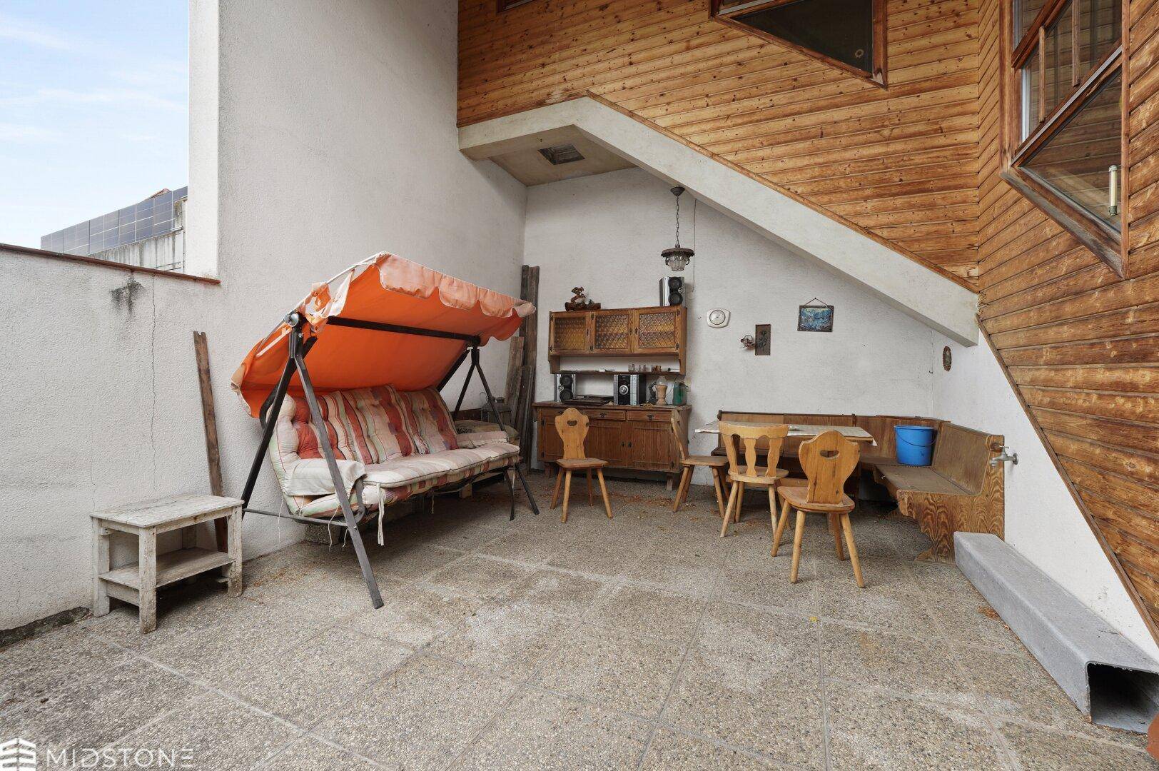 Überdachte Terrasse mit Schaukelbank und rustikalen Holzmöbeln, ideal für entspannte Stunden im Freien.