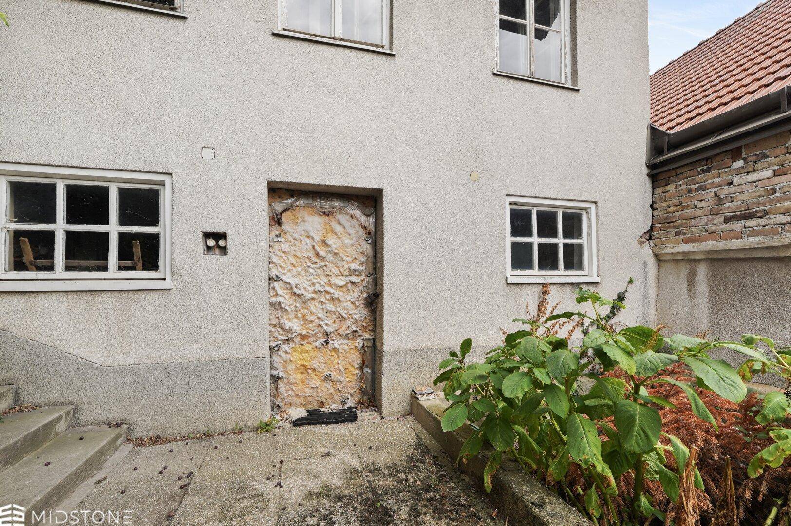 Fassade des Hauses mit einer alten, strukturierten Tür und mehreren Fenstern.