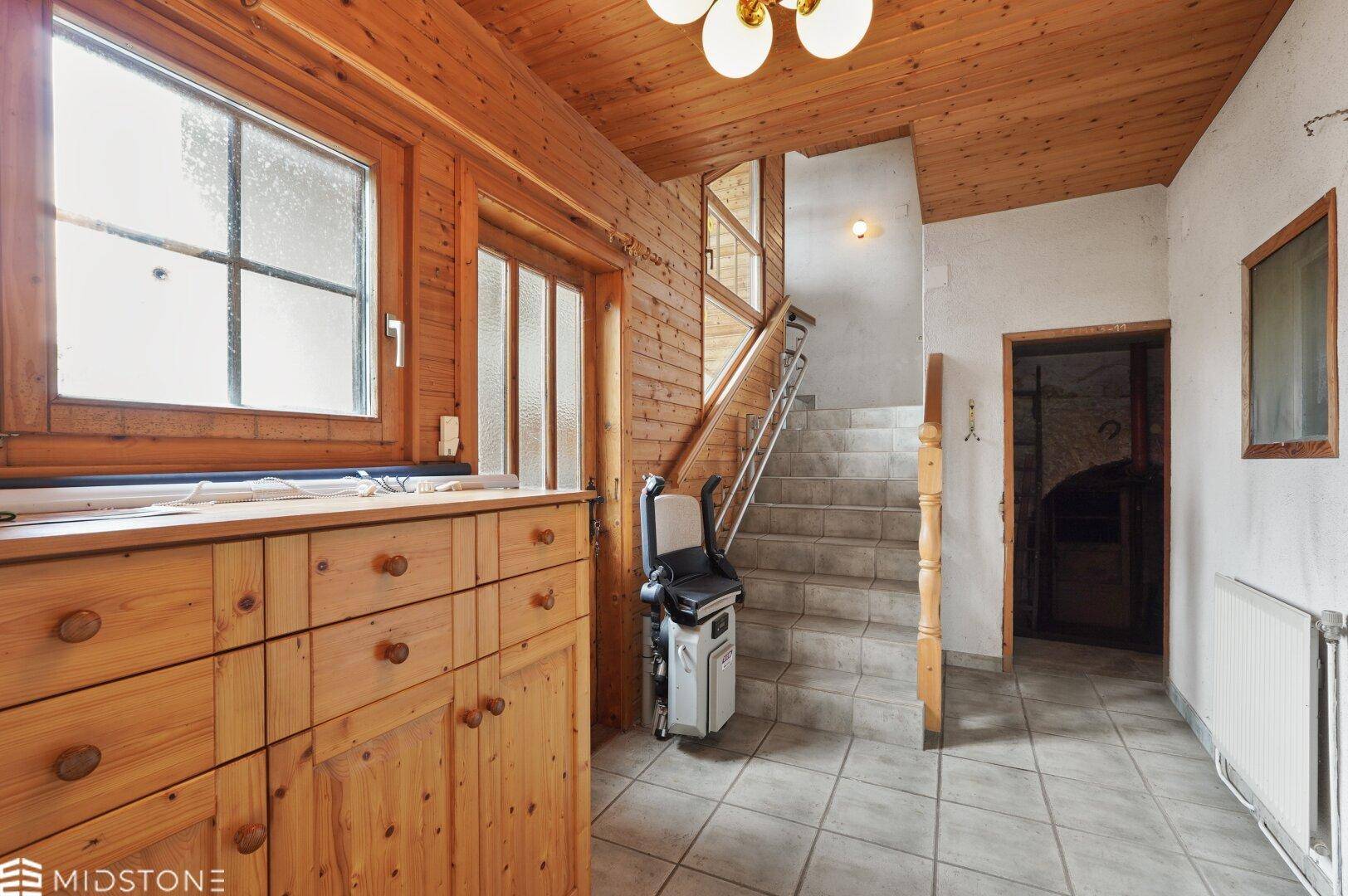 Rustikaler Eingangsbereich mit Holzvertäfelung, gefliestem Boden und Treppenlift zur oberen Etage.