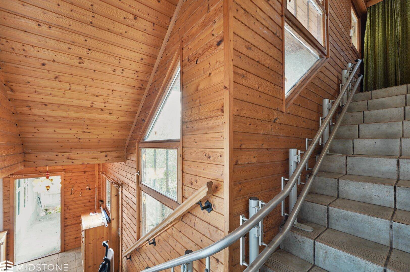 Holztreppe mit Metallgeländer und Holzvertäfelung an Wänden und Decke, mit Blick nach oben.