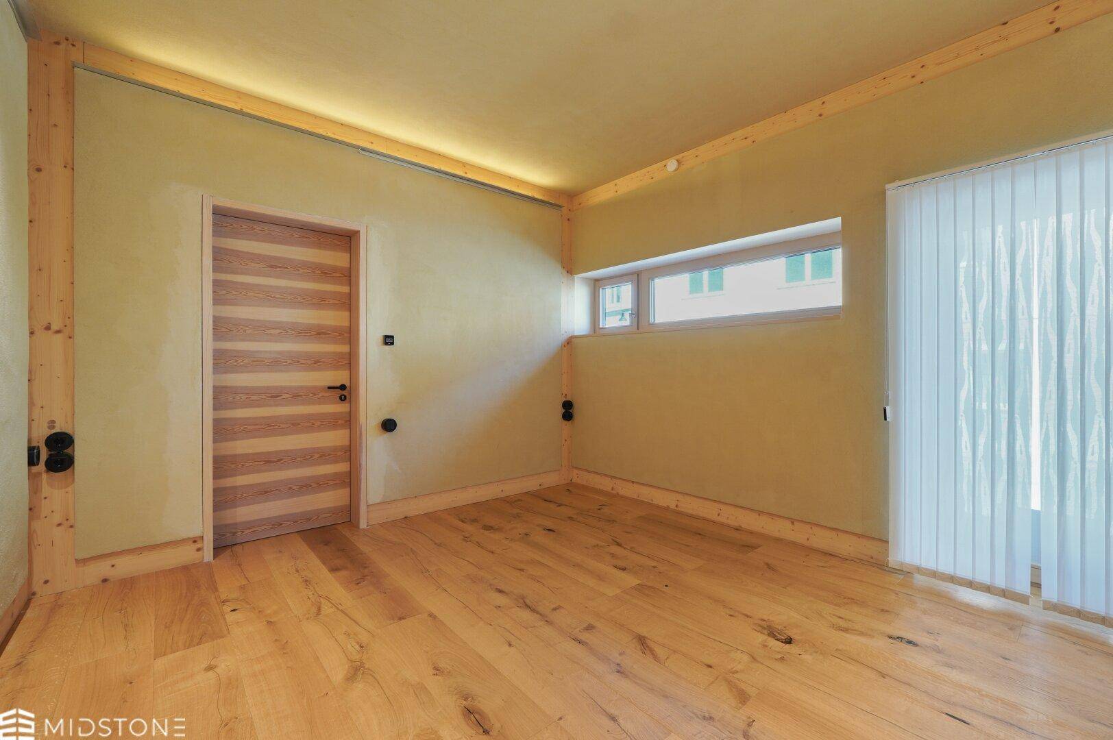 Geräumiger Raum mit Holzboden, Fenster und Holztür, ideal für verschiedene Wohnkonzepte.