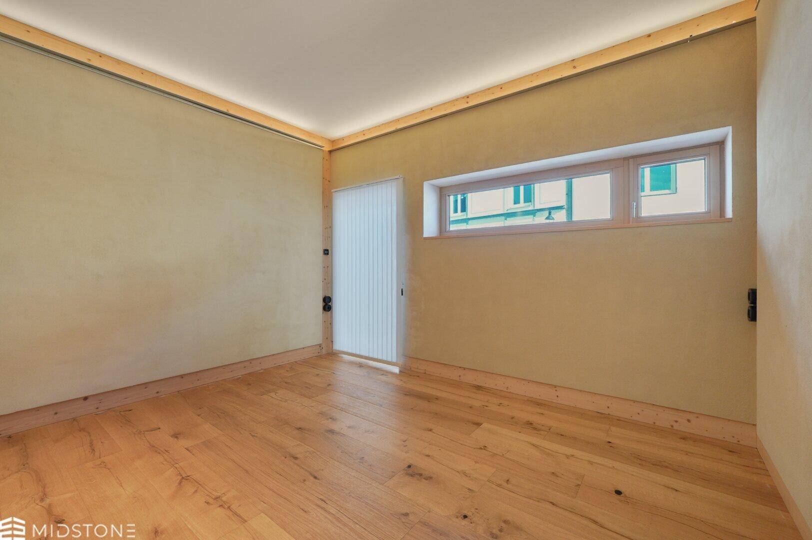 Lichtdurchfluteter Raum mit Holzboden und breitem Fenster, bietet flexible Gestaltungsmöglichkeiten.