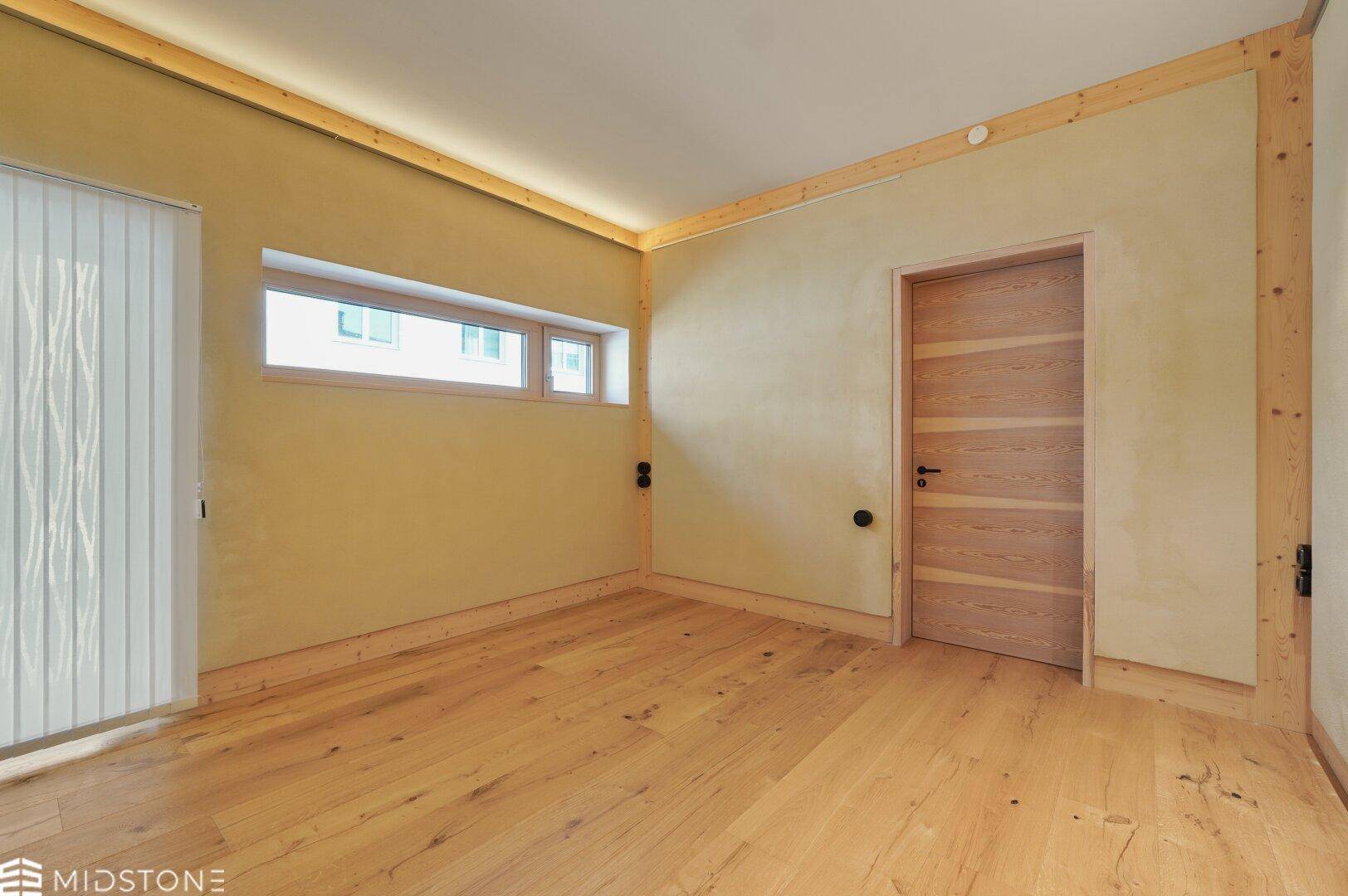 Heller Raum mit Holzboden, Fenster und Holztür, bereit für individuelle Einrichtungsideen.
