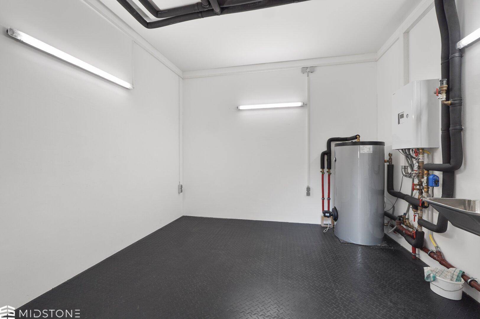 Funktionaler Technikraum mit Warmwasserboiler, Rohren und einem kleinen Waschbecken.