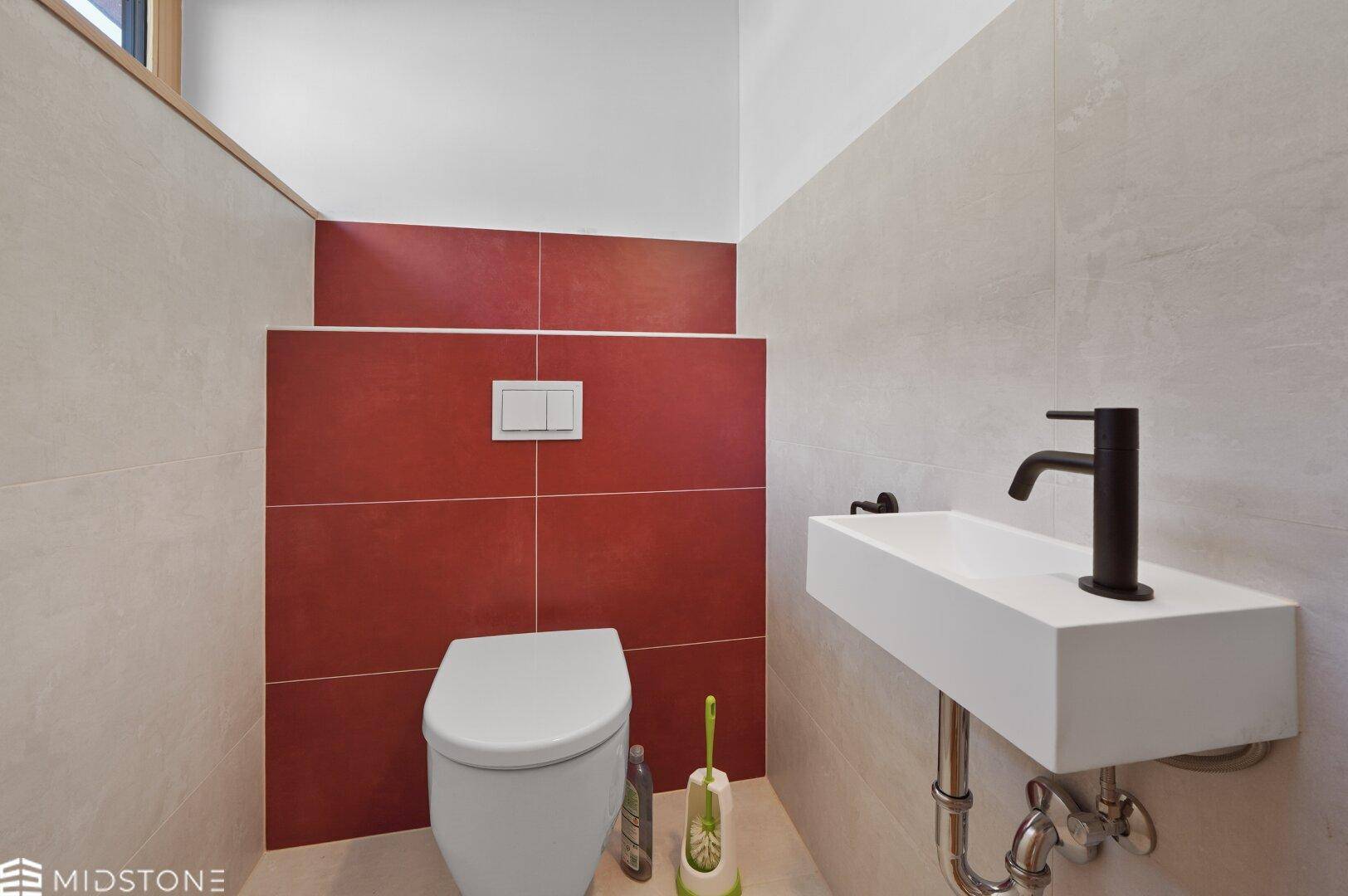Modernes Gäste-WC mit wandhängender Toilette, kleinem Waschbecken und roten Akzentfliesen.