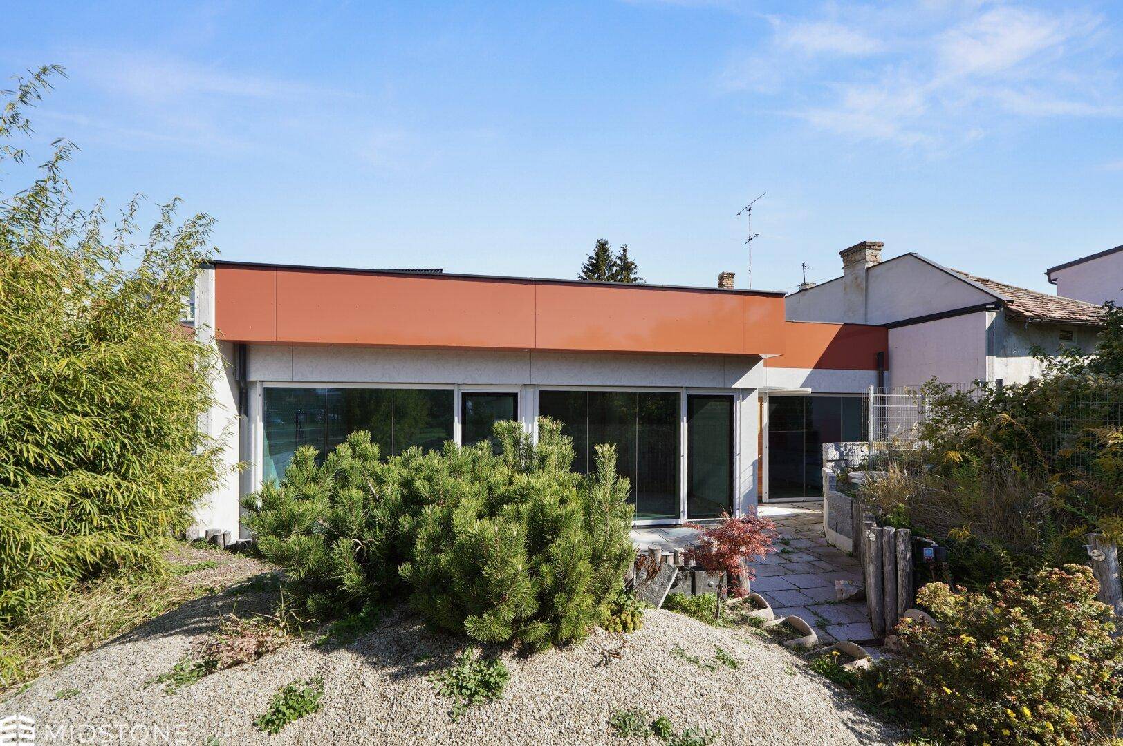 Moderne Architektur mit großen Fensterfronten und flachem Dach, umgeben von Grünflächen.