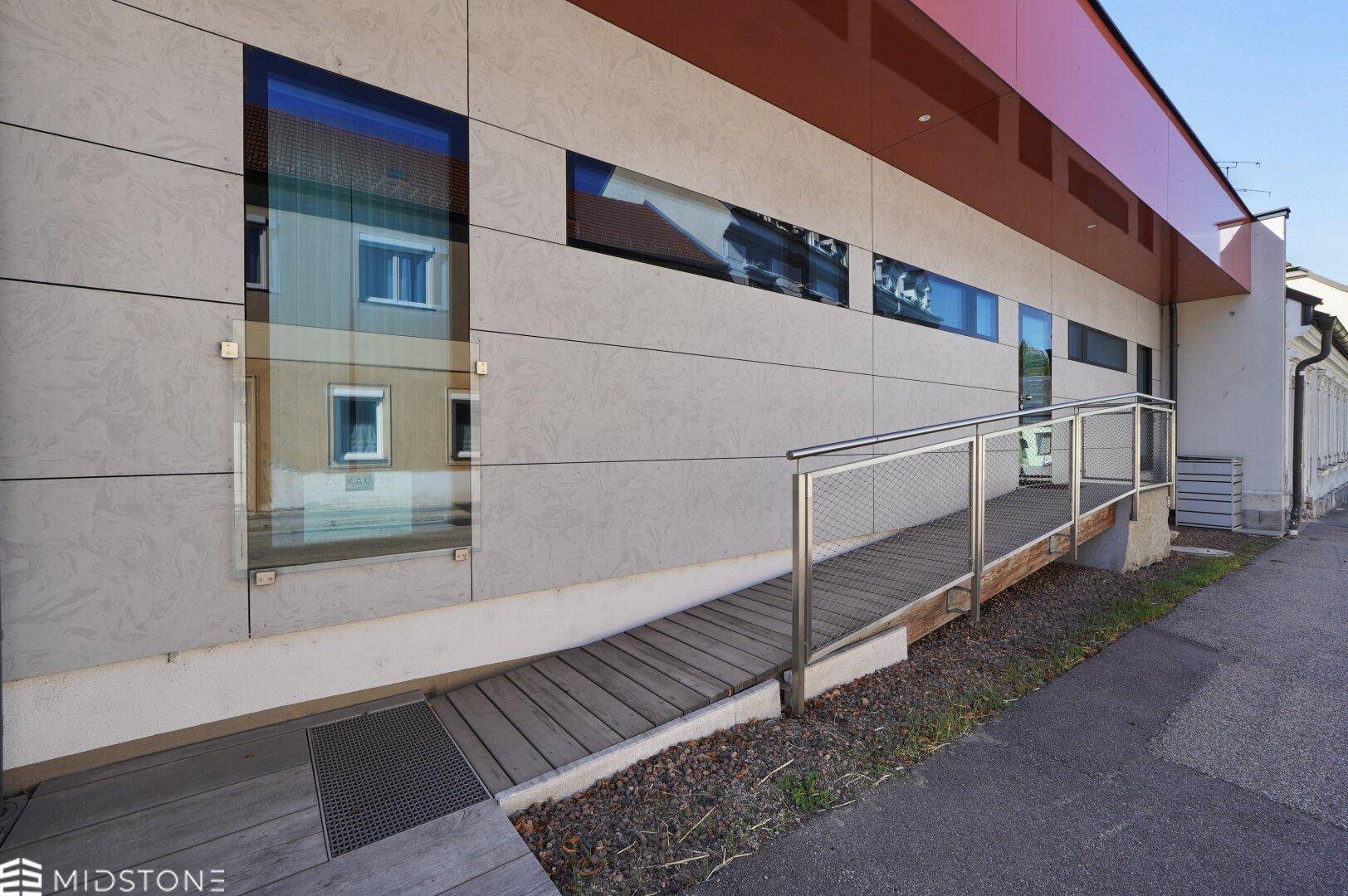 Moderne Gebäudefassade mit barrierefreier Rampe und großen Fensterflächen.
